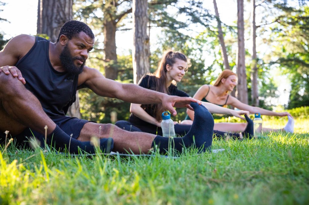 Fitness Group Warming up with Stretching Exercises on a Grassy Field.