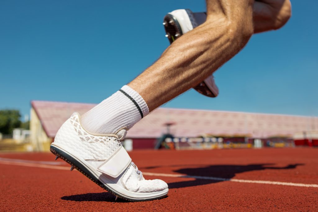 Close-up of athlete's legs starting on running track in sunlight